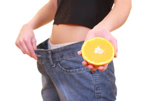 Image of a Woman Who Lostt Weight, wearing Jeans that are too big, and holding half an orange